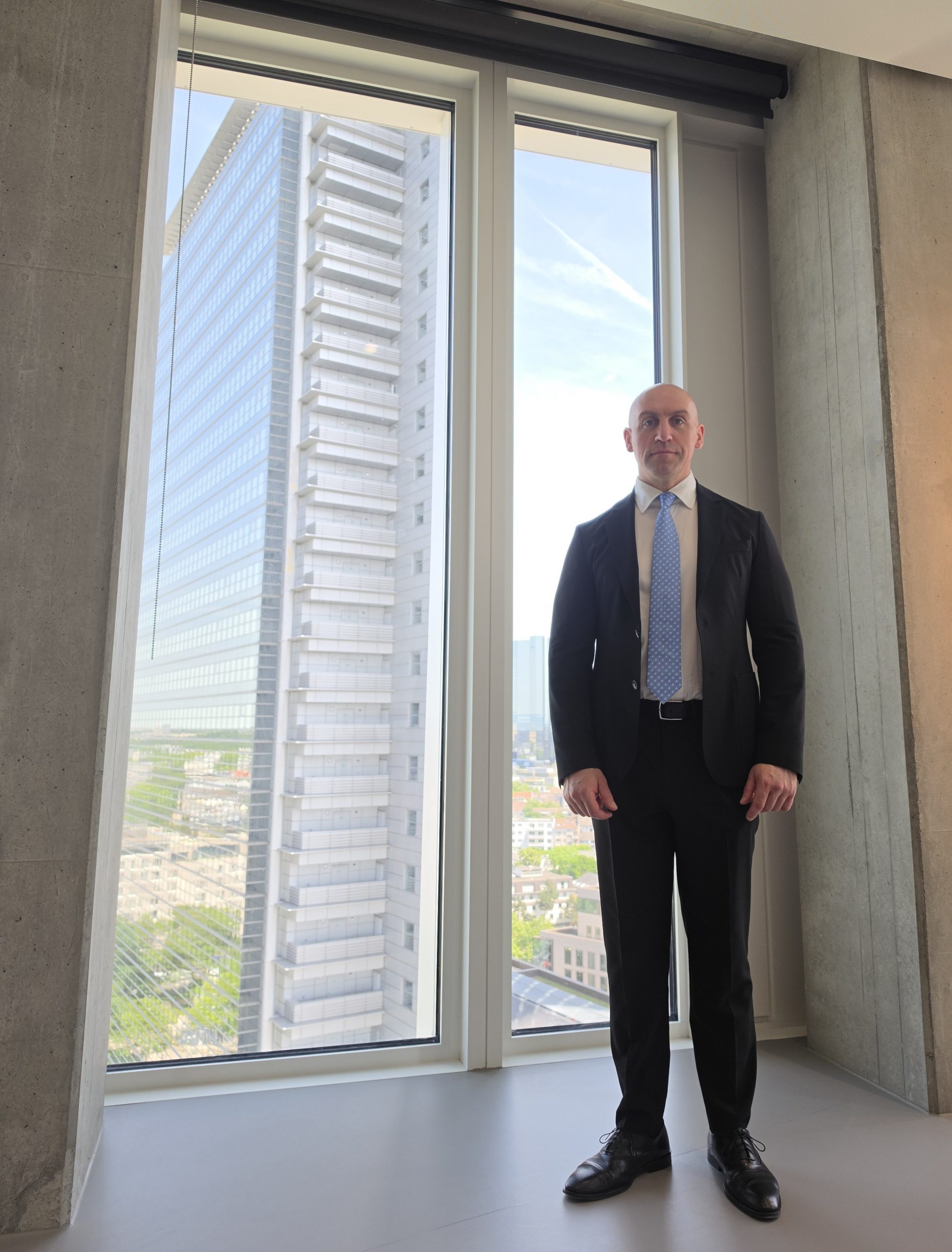 Ronny Kazyska in einem repräsentativen Hochhausinnenraum mit Beton- und Glasarchitektur sowie Blick auf Frankfurter Hochhausarchitektur zum Grundsatz Risikoprämie.
