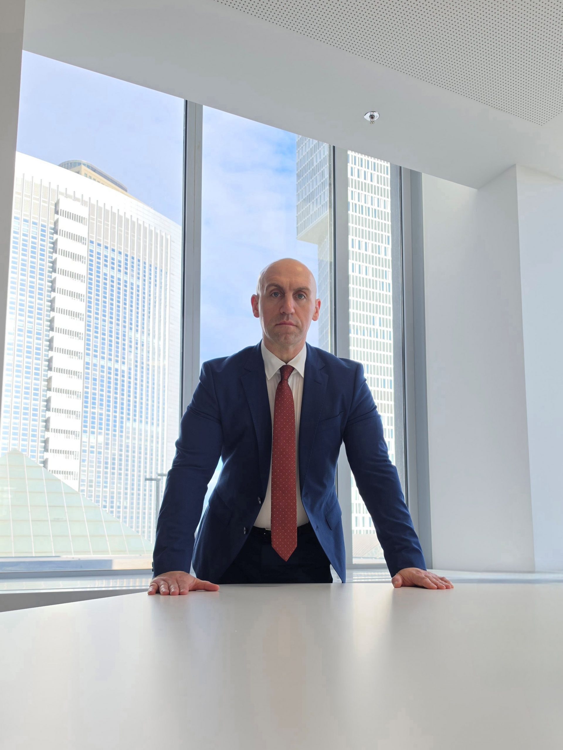 Ronny Kazyska an einem Konferenztisch in einem repräsentativen Hochhausinnenraum mit Blick auf die Frankfurter Hochhausarchitektur zum Grundsatz Transaktionsfähigkeit.