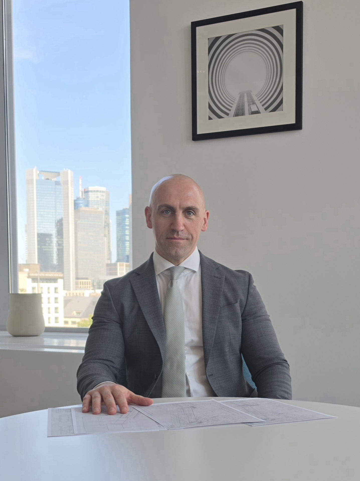 Ronny Kazyska an einem Konferenztisch mit Immobilienplänen in einem repräsentativen Hochhausinnenraum in Frankfurt zum Grundsatz Sachkunde in der Immobilienbewertung.