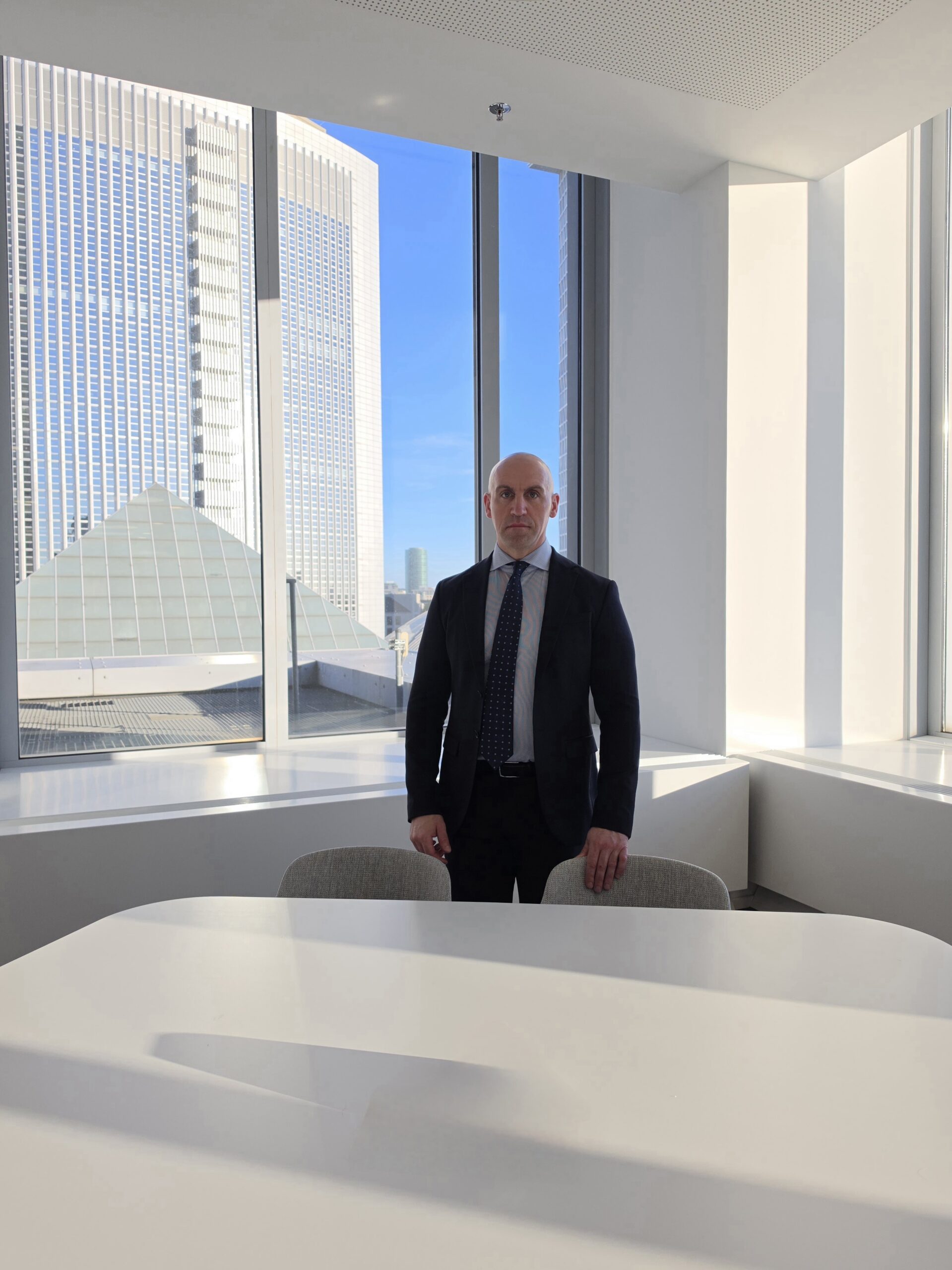 Ronny Kazyska in einem Konferenzraum mit Blick auf die Frankfurter Hochhausarchitektur zum Grundsatz Abschlusssicherheit bei Immobilientransaktionen.