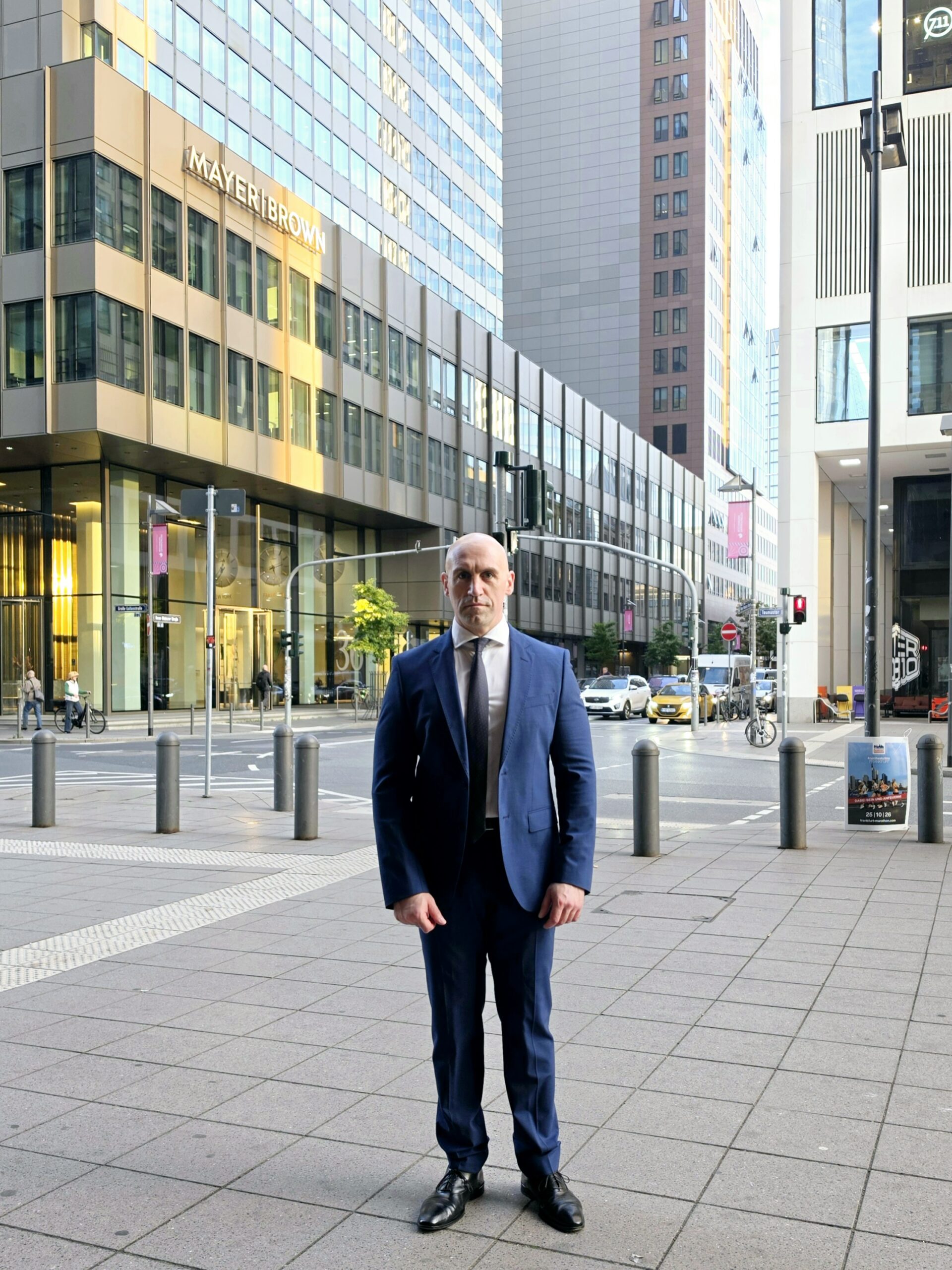 Ronny Kazyska im Anzug im Frankfurter Bankenviertel vor moderner Büro und Hochhausarchitektur.